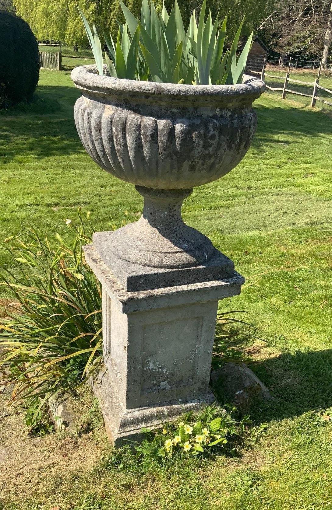 A pair of reconstituted stone campana shaped garden urns on square plinths, diameter 58cm height 129cm